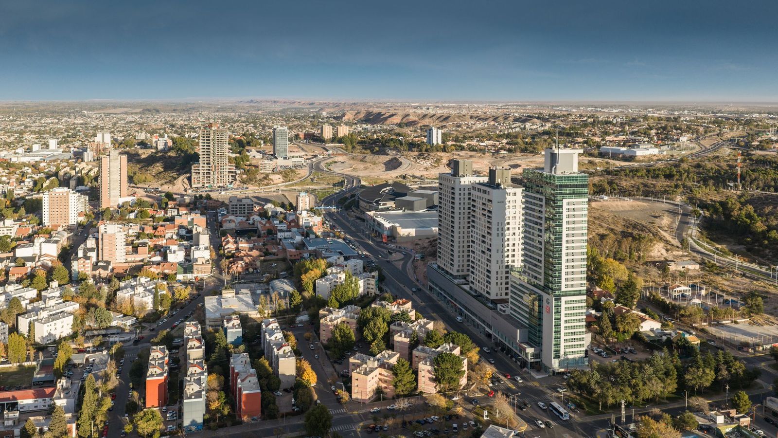 Vista aérea de torres y avenidas en Neuquén Capital, con la barda al fondo