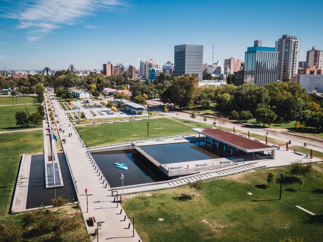 Parque urbano en Neuquén Capital, con espejo de agua y el skyline al fondo